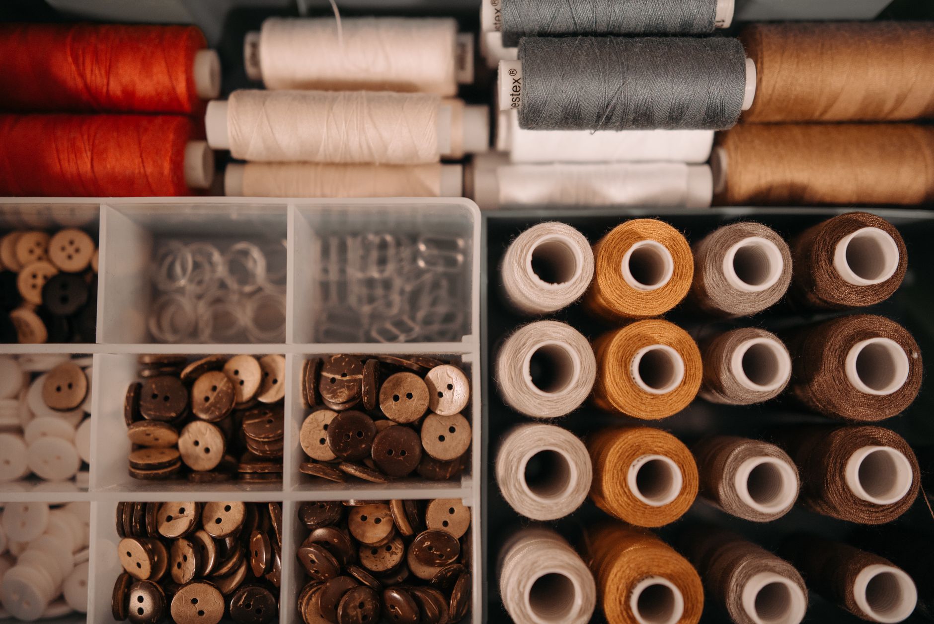 variety of sewing threads and buttons in a box with divider