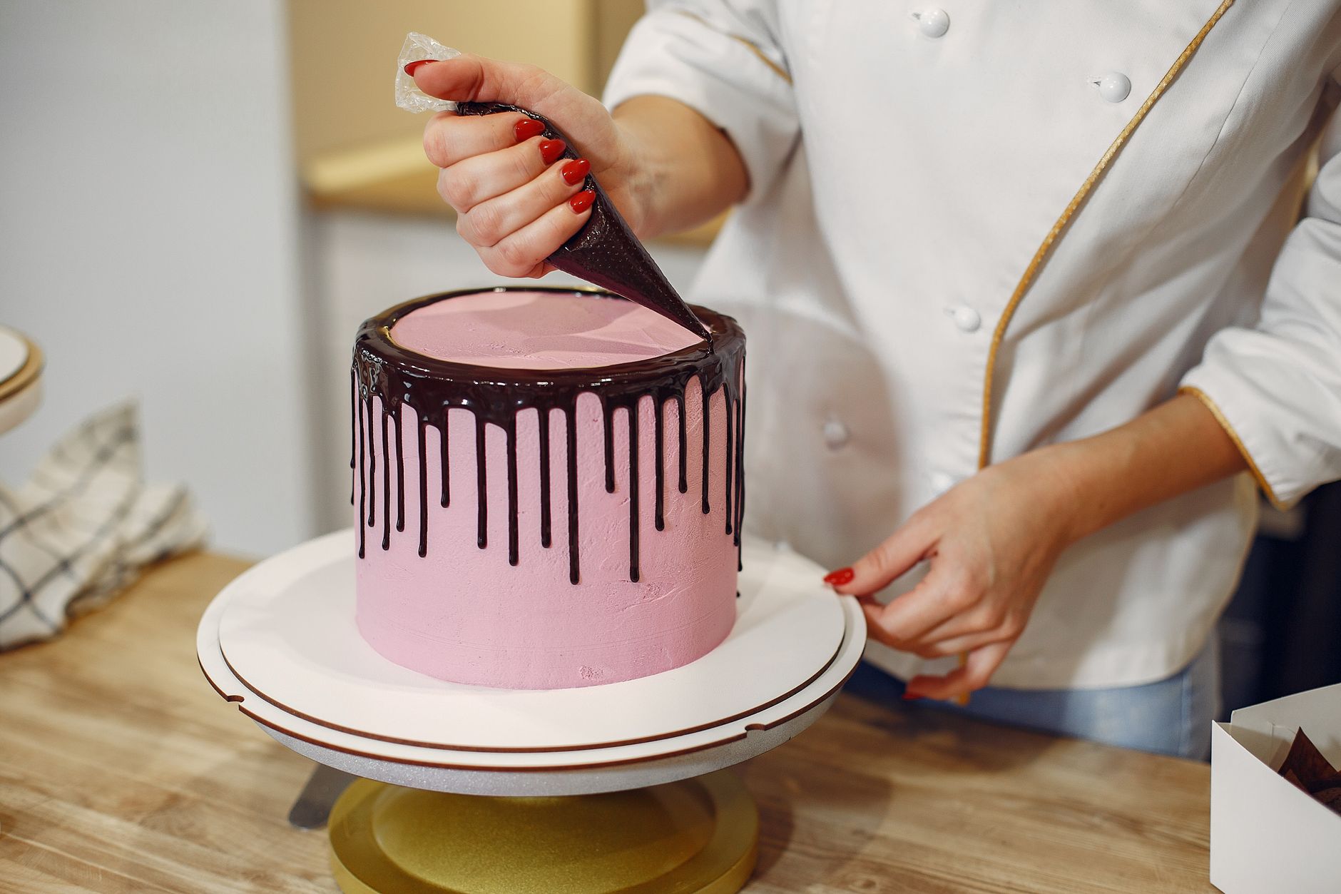 crop woman pouring melted chocolate on sides of cake in confectionery